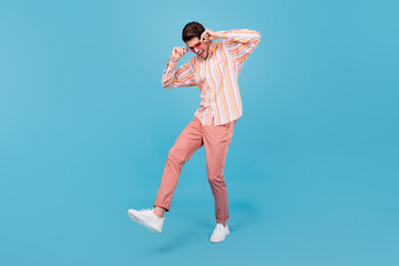 Full length photo of young man happy positive smile have fun hands touch sunglass isolated over blue color background