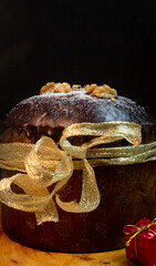Panettone on a wooden table with a black background surrounded by Christmas ornaments and a little box with gift