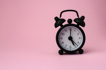 A small alarm clock on pink background, 5 o'clock with copy space