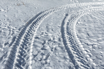Fototapeta na wymiar Traces of a wheeled tractor in the snow. Winter snow patterns.