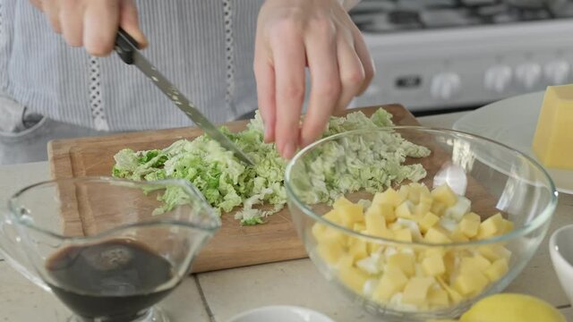 Woman chopping chinese cabbage for salad. Recipe for cooking tuna salad with egg, chinese cabbage, cheese and kiwi. Process of preparing. Close-up of healthy breakfast or lunch. 4K, UHD