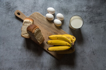 Breakfast food items bread, milk, eggs and bananas on a wooden board on a background with use of selective focus 