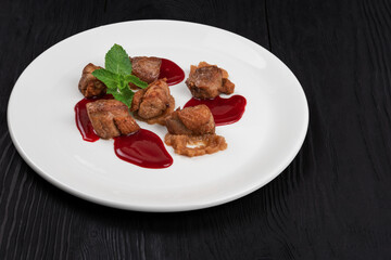 Delicacy Fried pork meat with zucchini puree and berries sauce decorated with mint on white plate on black wooden background