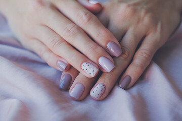 Women - hands with beautiful manicure on a background of silk fabric. Autumn trend, polish the beige and quail pattern on the nails with gel polish, shellac. Copy space.