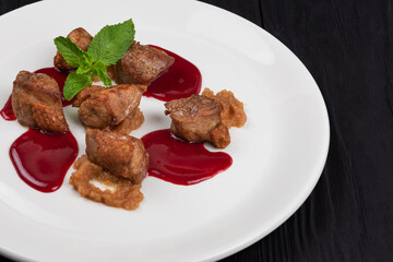 Delicacy Fried pork meat with zucchini puree and berries sauce decorated with mint on white plate on black wooden background