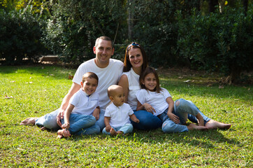 Fototapeta premium Portrait of happy parents with their three children lying in the park. The eldest daughter is a transgender girl. Concept of family happy united family with children.