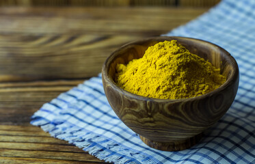 Turmeric powder in a wooden bowl on a blue napkin and a wooden background. Turmeric close -up.