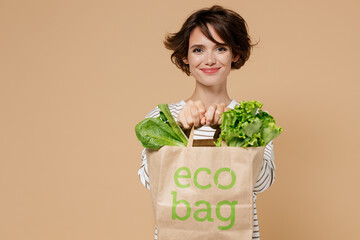 Young smiling caucasian european happy fun vegetarian woman 20s in casual clothes hold paper bag with vegetables after shopping look camera isolated on plain pastel beige background studio portrait. - Powered by Adobe