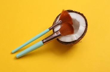 Makeup brushes with coconut on yellow background