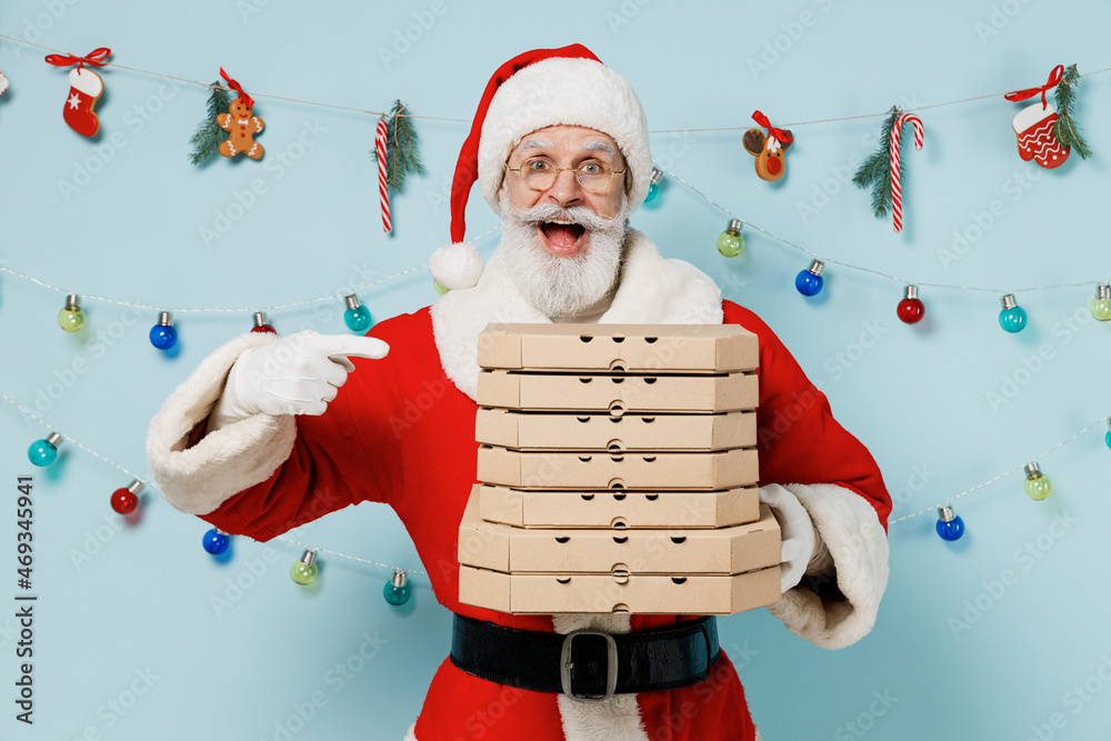 Wall mural Old Santa Claus man 50s wears Christmas hat red suit hold point on italian pizza in cardboard flatbox isolated on plain blue background studio. Happy New Year 2022 celebration merry ho x-mas concept.