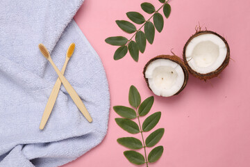 Fototapeta na wymiar Hygiene, oral care concept. Eco toothbrush, coconut with green twigs and towel on pink background