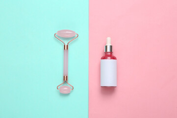 Bottle of face serum, massage roller on blue pink background. Top view