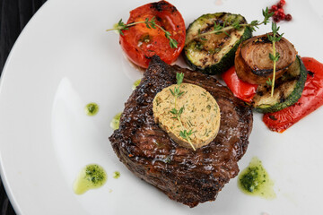 Grilled black angus strip loin steak with vegetables on white plate on black wooden background