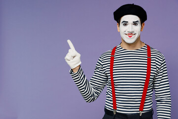 Fototapeta na wymiar Happy charismatic fun young mime man with white face mask wear striped shirt beret pointing aside on workspace area copy space mock up isolated on plain pastel light violet background studio portrait