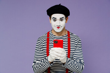 Charismatic amazing marvelous ecstatic young mime man with white face mask wear striped shirt beret hold in hand use mobile cell phone isolated on plain pastel light violet background studio portrait