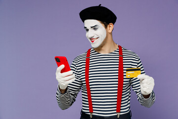 Satisfied young mime man white face mask wears striped shirt beret using mobile cell phone hold...