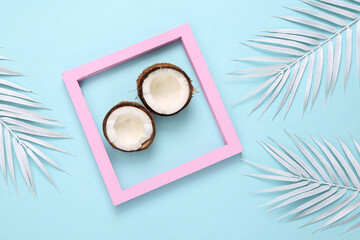 Obraz na płótnie Canvas Coconuts in pink frame with white palm leaves on blue background. Minimal tropical background. Creative layout