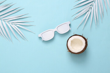 Obraz na płótnie Canvas White sunglasses, coconut and palm leaves on blue background. Minimal travel, tropical layout. Top view