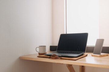 Laptop workspace on wooden desk by the windows with morning light.