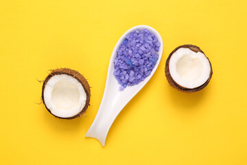 Spoon with sea bath salt and coconut on yellow background. Top view