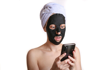Young attractive woman with black cleansing cosmetic mask using gsmartphone on white background