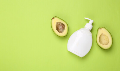 A bottle of cream with avocado halves on a green background. Natural cosmetics concept. Skin care