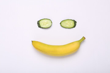 Creative composition of cucumber and banana in the shape of face on white background