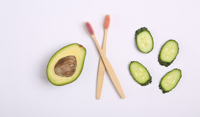 Bamboo toothbrushes with avocado and cucumber slices on a white background. Top view