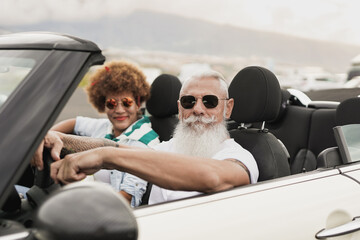 Happy senior couple looking on camera during road trip with convertible car - obrazy, fototapety, plakaty