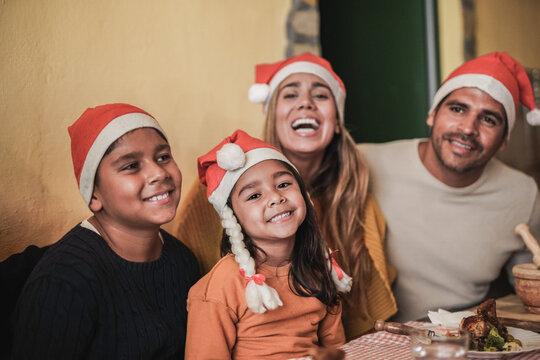 Happy latin family having fun at christmas dinner while wearing santa claus hats