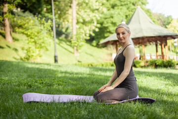 Young attractive blonde yogi woman sitting on the mat in the park