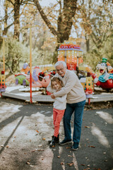 Grandfather having fun with his little granddaughter in the amusement park