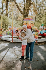 Poster Grandfather having fun with his little granddaughter in the amusement park © BGStock72