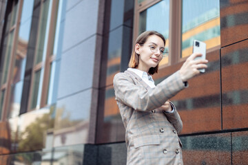 Stylish young business woman taking a selfie on a smartphone against the background of a business building