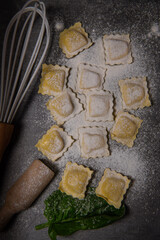 Tasty raw ravioli with flour and spinach on dark background, process of making italian ravioli