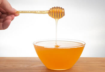 fresh honey dripping from a spoon into a transparent plate on a white background. organic vitamin health food