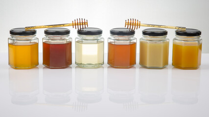 Hexagonal jars with different types and colors of fresh flower honey and a honey spoon. vitamin...