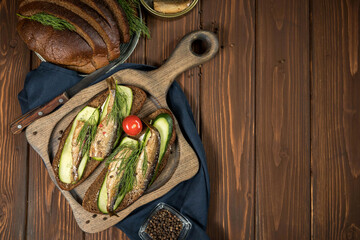 Sandwiches with smoked  sprats  on a wooden server and wooden background . Sprat sandwich with a copy space