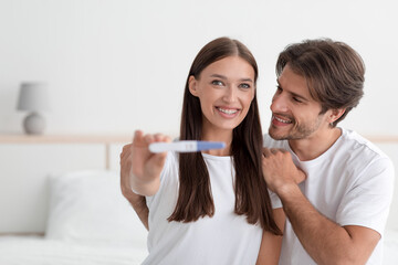 Satisfied glad attractive millennial caucasian couple rejoice result and show pregnancy test in bedroom