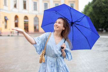 Young smiling woman in dress with umbrella waiting for rain in the city