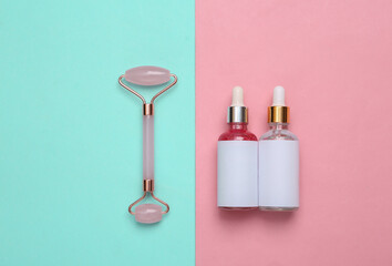 Beautiful composition of mockup serum bottle, pink face roller on pink blue background. Face massage set. Creative trendy beauty flat lay