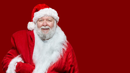 Closeup image of a happy Santa Claus dressed in a red coat and a hat, keep a bag on his back, isolated red background.