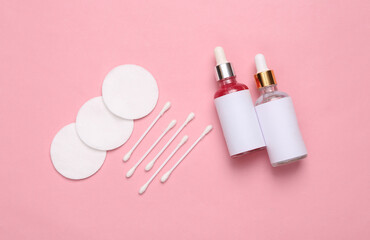 Face serum bottles, cotton pads and sticks on a pink background. Facial skin care, hygiene. Flat lay composition