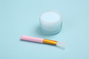 Jar of face cream and brush on blue background