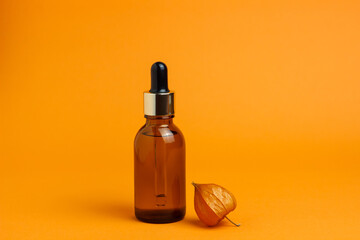 Glass brown cosmetic jar with a pipette on an orange background. Physalis flower. Minimalism. Place for your text.