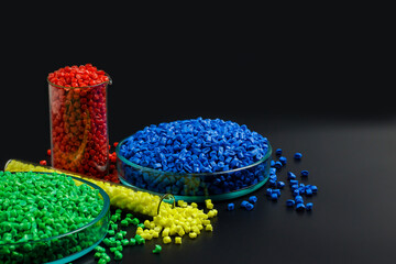Blue, yellow, red granules of polypropylene, polyamide in a test tube and a petri dish. Black background. Plastic and polymer industry, industry. Microplastic products.