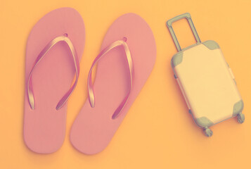 Travel or beach resort flat lay. Mini plastic travel suitcase and flip flops on yellow background. Minimal style. Top view