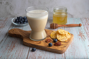 Glass of vegan oat milk on an olive wooden board, with honey and a bowl of blueberries, concept healthy eating.