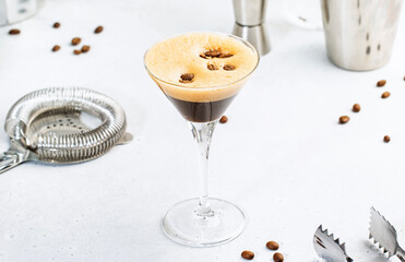 Espresso martini, trendy alcoholic cocktail with vodka, coffee liqueur, syrup and ice, black background, bar tools