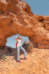 Tourist woman with backpack walks along a trail in a deserted canyon with majestic arch of red rocks. Hiking path and the dangers of solo trekking